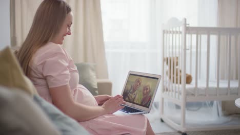 pregnant woman sitting on sofa and using a laptop making a video call with his parents