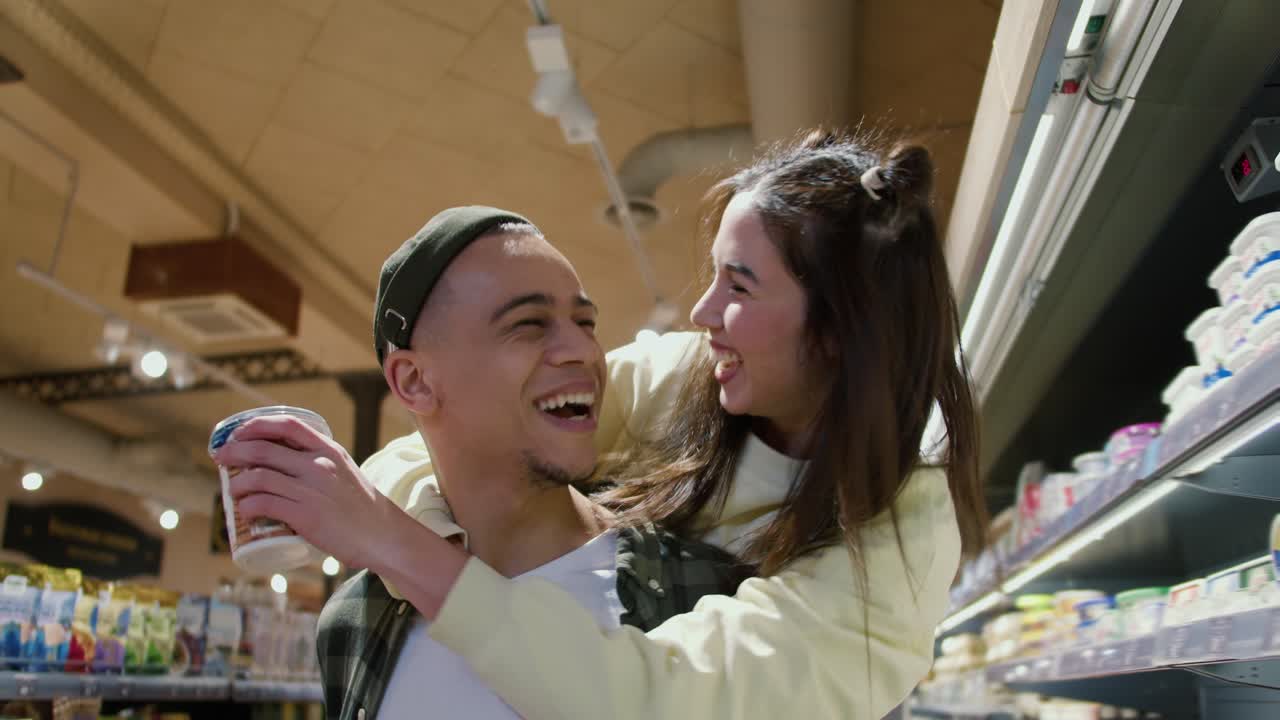 재미있는 젊은 성인 남자친구가 슈퍼마켓에서 제품을 선택하면서 여자친구를 등에  ⁇ 고 있습니다.