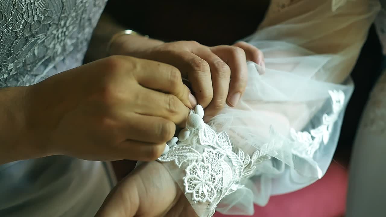 Bridesmaid helping bride to fasten buttons in the hands