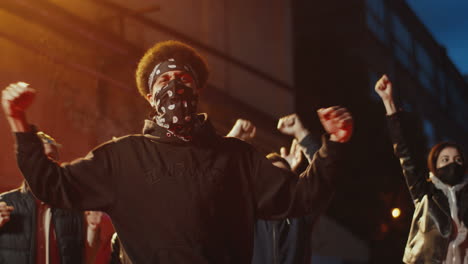 african american man with scarf on his face yelling and throwing gas in a protest with multiethnic group of people in the street