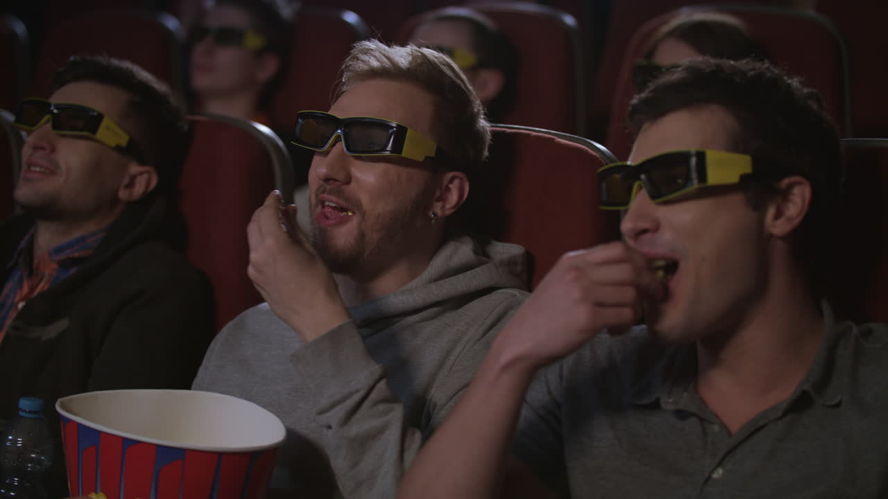 amigos del hombre comiendo palomitas de maíz en el cine 3d película. los hombres se divierten en el cine