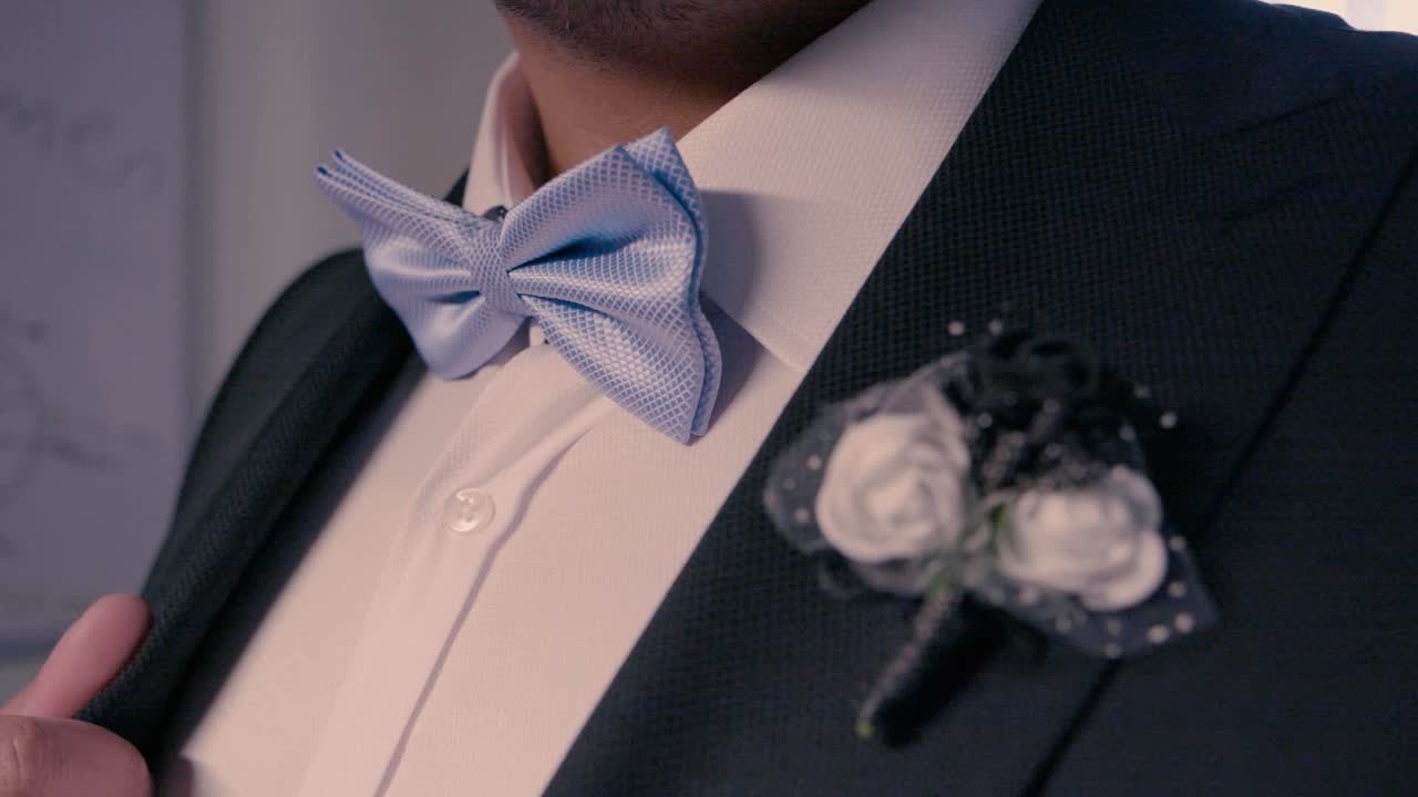 toma estática de un novio con traje y corbata de moño con un reloj noble en el brazo que se está poniendo la chaqueta de fumar