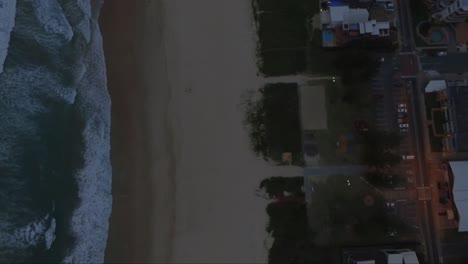 birdseye view of beach and ocean next to a road with cars and houses at dusk