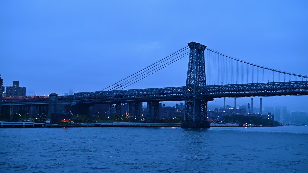 Le luci illuminano il ponte di Williamsburg al crepuscolo a New York, USA. Vista sul paesaggio fluviale. Profilo della città sfocato sullo sfondo.