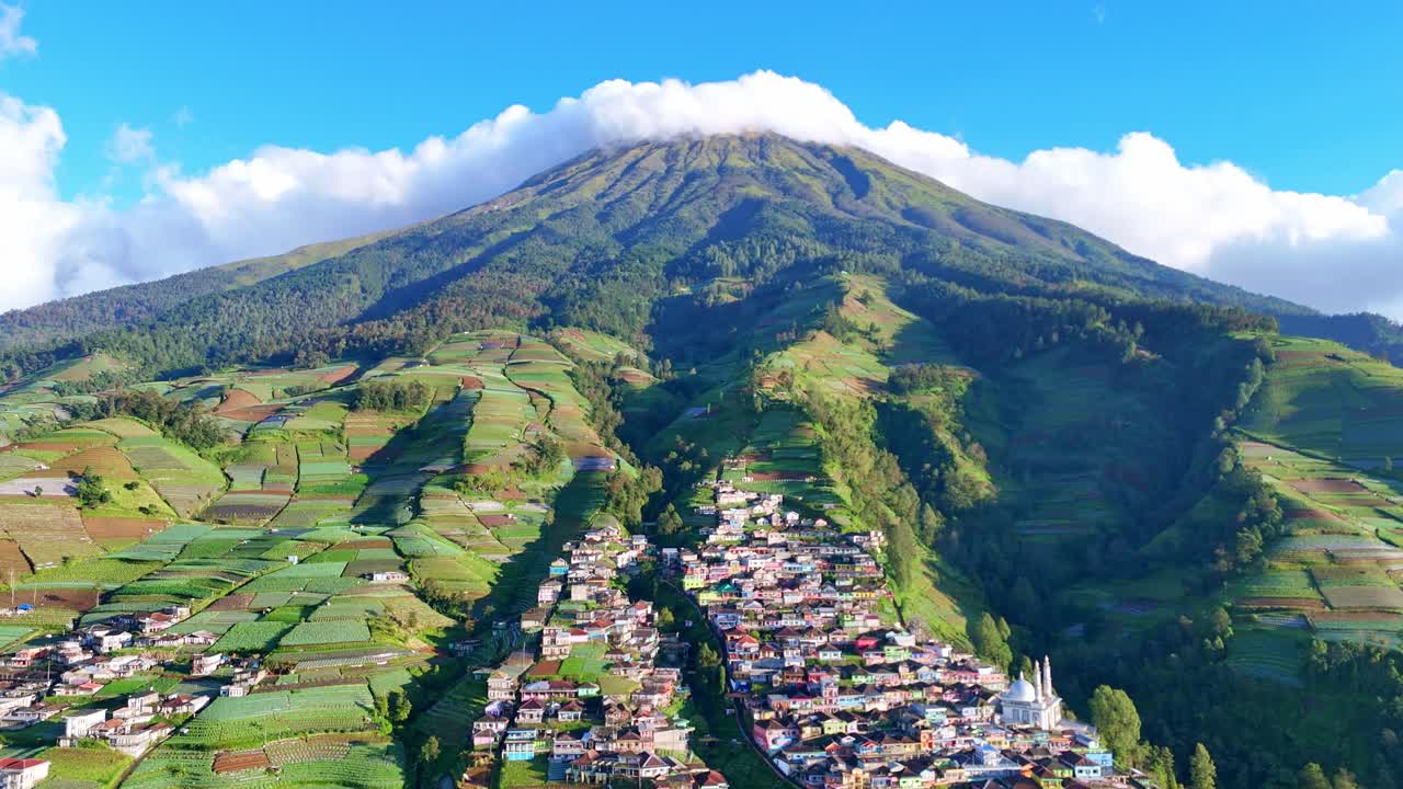 Stunning aerial footage of a mountain valley village surrounded by layered farmlands and vibrant green hills. Nepal Van Java Village, Mount Sumbing, Indonesia
