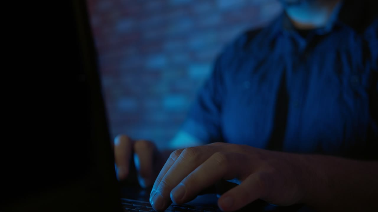 Man Typing on Laptop Keyboard in Dark Room with Blue Light