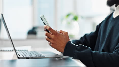 man using phone and laptop at desk in office