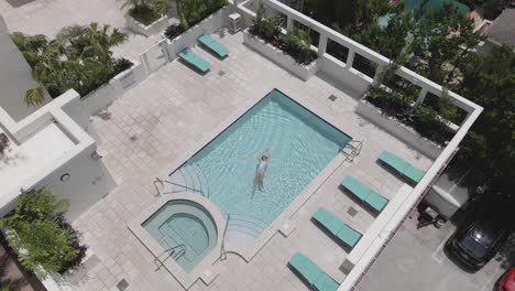Aerial-rises-as-young-woman-enjoys-floating-in-private-swimming-pool