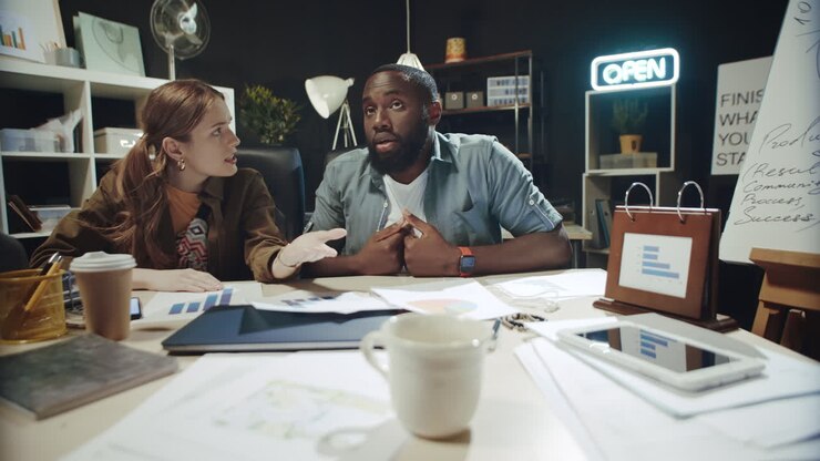 Frustrated multi ethnic business couple discussing project in hipster office.