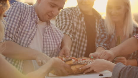 a company of young people parses pieces of hot pizza. this is a rooftop party with a beer.