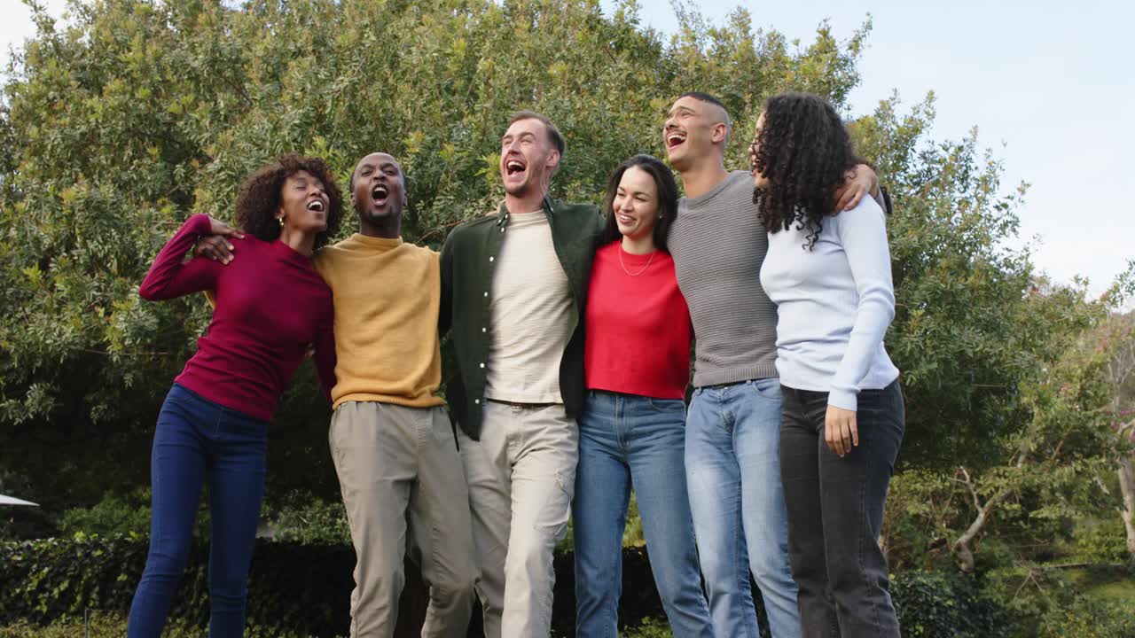 Diverse friends exchanging laughs, linking arms, tapping feet in park beside bench celebrating bond