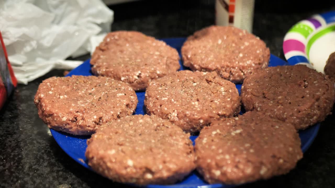 Seasoning plant based burger patties on a blue plate for a summertime barbecue cookout, wide shot 60 frames per second 4k