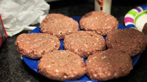 seasoning plant based burger patties on a blue plate for a summertime barbecue cookout, wide shot 60 frames per second 4k