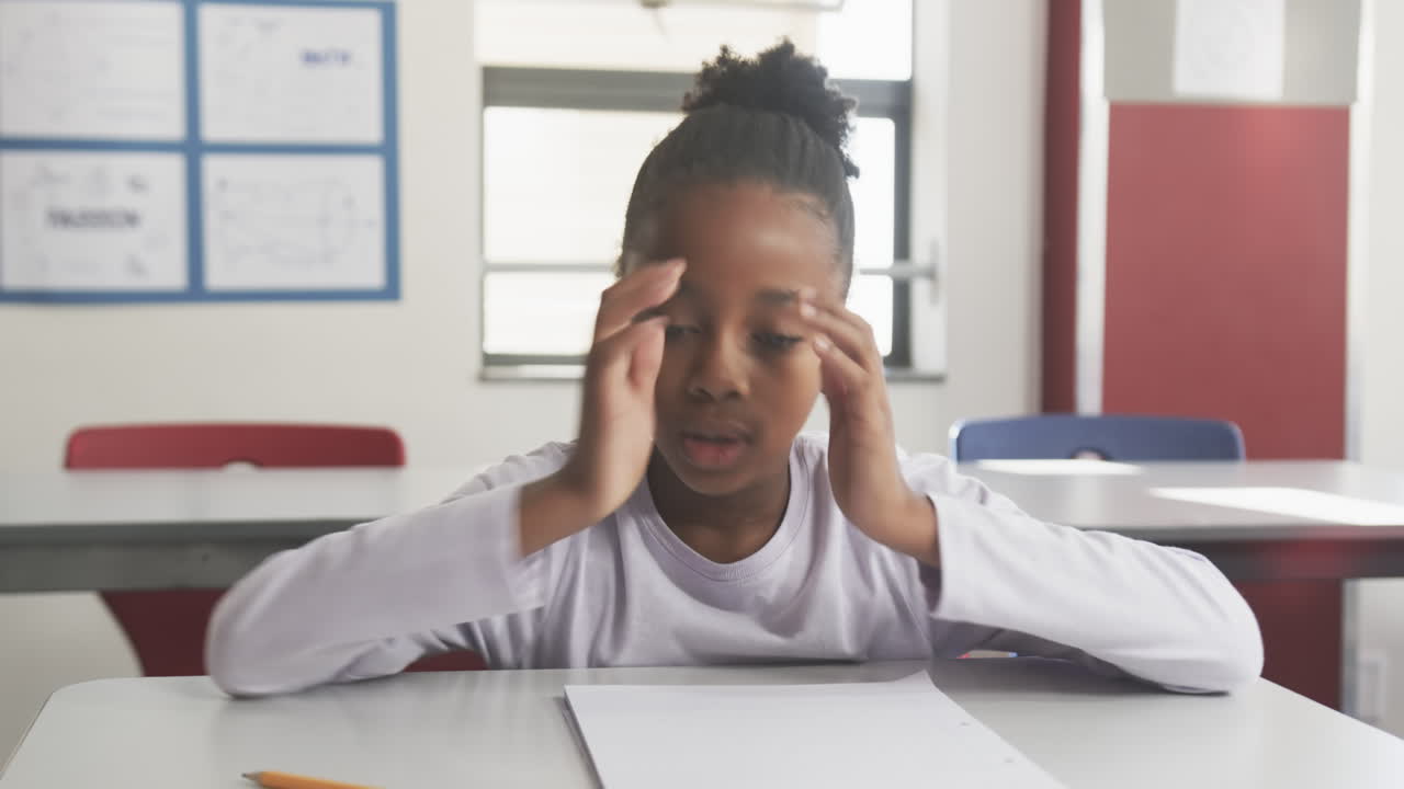 A scuola, uno studente si copre il viso con le mani mentre è seduto alla scrivania in classe.