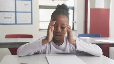 in school, student covering face with hands while sitting at desk in classroom