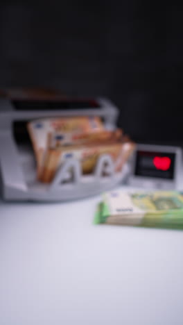 orange banknotes are rotated and counted in money counting machine. male hand puts the counted stack near another one on the desk. vertical video.