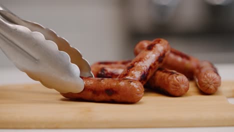 setting a sausage link down on cutting board with tongs for breakfast in bright kitchen in slow motion 4k