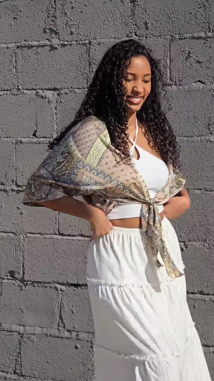 An elegant young woman is posing in a stylish outfit against a unique textured wall