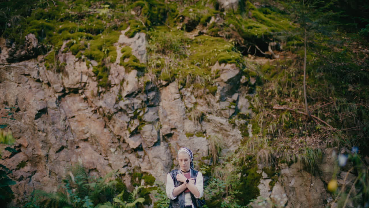 mujer pensativa con un libro de pie contra las rocas