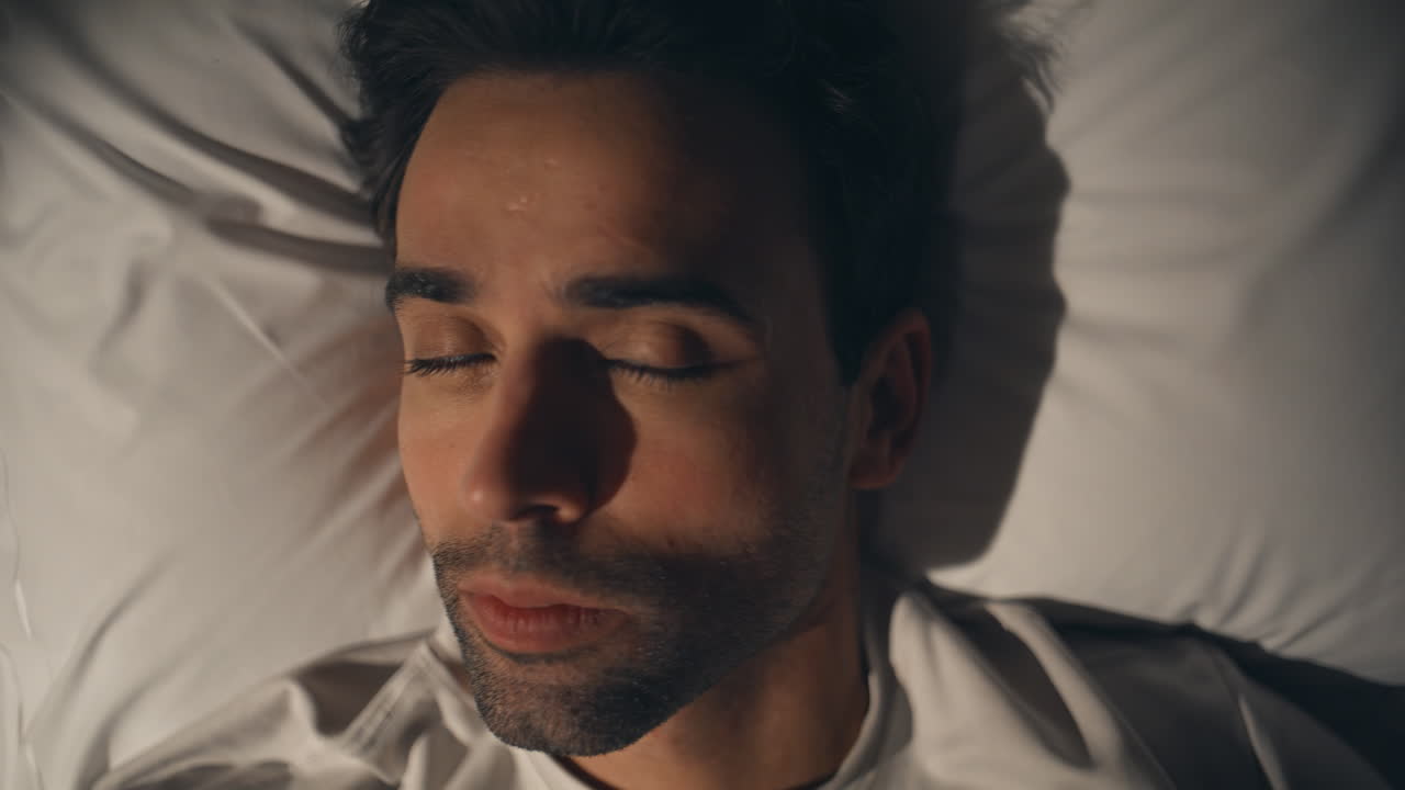 Thinking man lying pillow looking up at night closeup. Calm unshaved guy resting