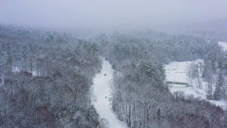 flying high above a road and river winding through a forest during a snow storm slow motion aerial