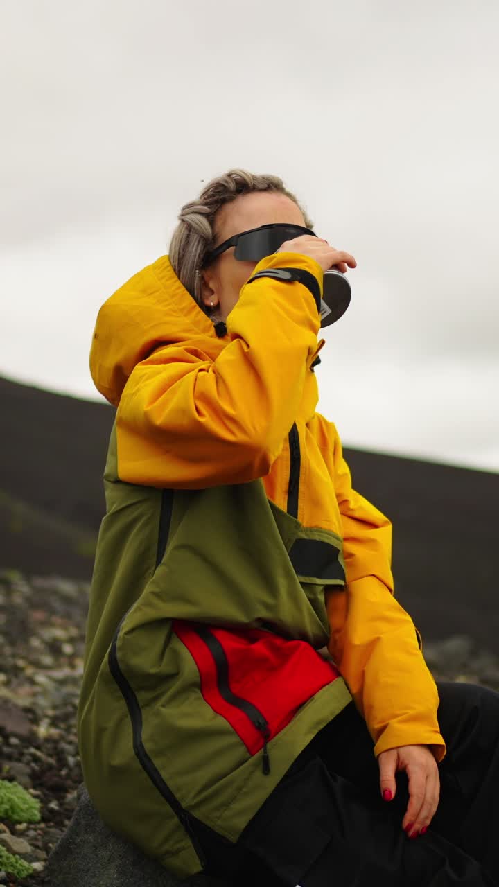 Woman in Yellow Jacket Drinking from Cup in Rocky Landscape