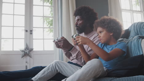 black middle aged father and his pre teen son sitting on the floor in their living room eating and playing video games together, close up