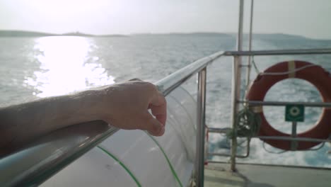 hand resting on a boat's metal rail while sailing next to islands