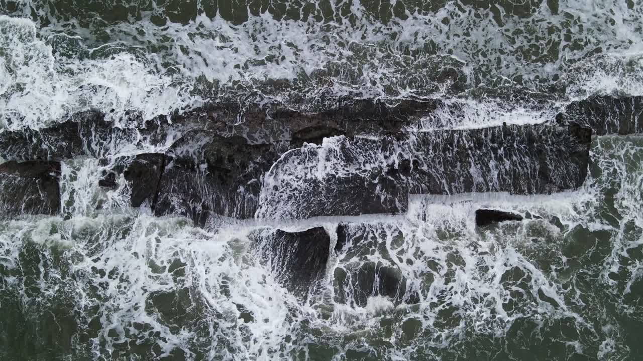 Aerial top-down view of murky ocean waves crashing against rugged coastal rocks during a stormy day at Catanduanes, Philippines
