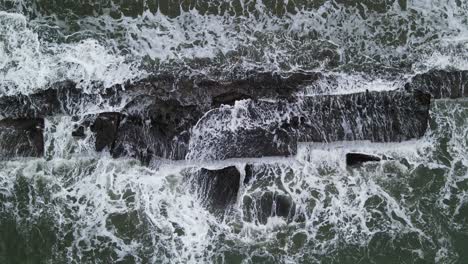 aerial top-down view of murky ocean waves crashing against rugged coastal rocks during a stormy day at catanduanes, philippines