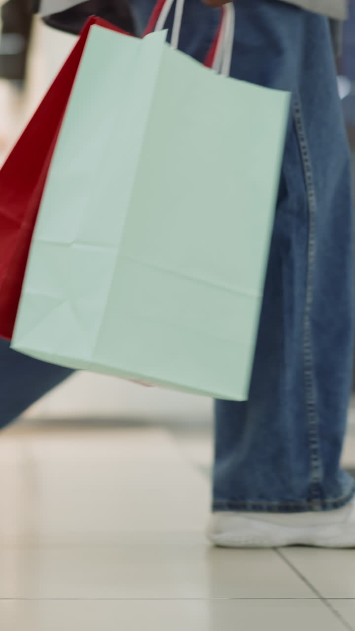 Woman legs in jeans and sneakers walking across mall closeup slow motion. Lady customer holds shopping bags after visiting fashion stores. Hobby and leisure