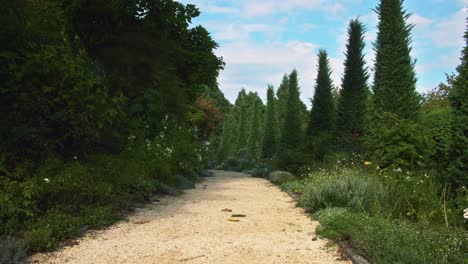 centered orange gravel european pathway turns the curve, left and right along the track surrounded by mediterranean green shrubs and plants, blue clean sky above filled with some summer clouds