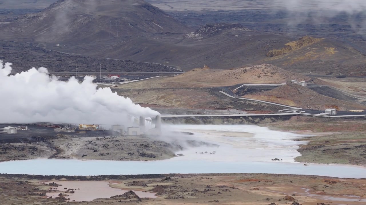 Svartsengi geotermiska kraftverk avger tät ånga bredvid mineralrikt vatten och vulkaniska sluttningar nära Grindavikurbaer, Reykjanes, Island, med industrivägar som korsar landskapet