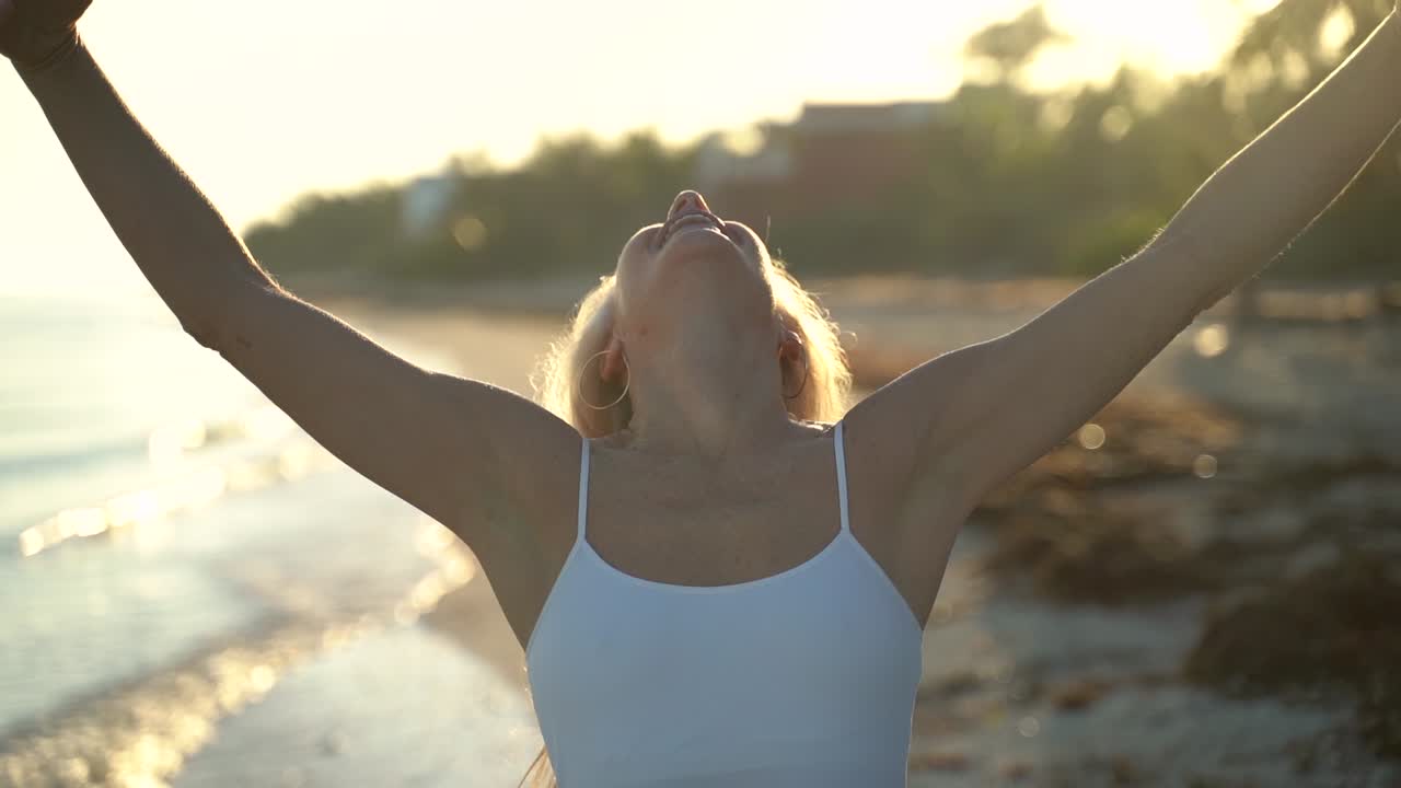 Slow motion of mature woman throwing hair back, putting her arms out looking up to sky and then smiling at camera