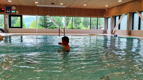 boy with autism playing and flapping hands alone in swimming pool - static clip showing boy having fun and doing weird hand movements