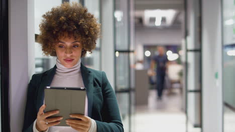 Evening-Shot-Of-Businesswoman-Standing-In-Corridor-Of-Modern-Office-Using-Digital-Tablet