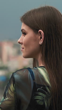 happy young woman tourist with long brunette hair in elegant dress with print enjoys large city view on spring day slow motion close view