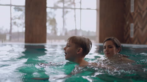 Piscina-Pública-Para-Familias-Con-Niños-La-Mujer-Le-Está-Enseñando-A-Nadar-A-Su-Hijo-El-Niño-Está-Nadando