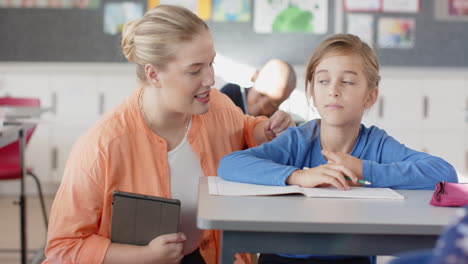 in school, female teacher helping student with writing assignment in classroom