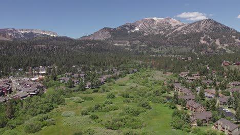 4k drone footage slow pan right and zoom out of beautiful mammoth mountain in the summertime with a view of a lush green meadow and cabins