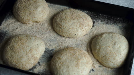 Top-down-slow-motion-shot-of-sourdough-bread-ready-to-make-homemade-pizzas,-tray-of-sourdough-bread-being-taken-away-ready-to-be-baked