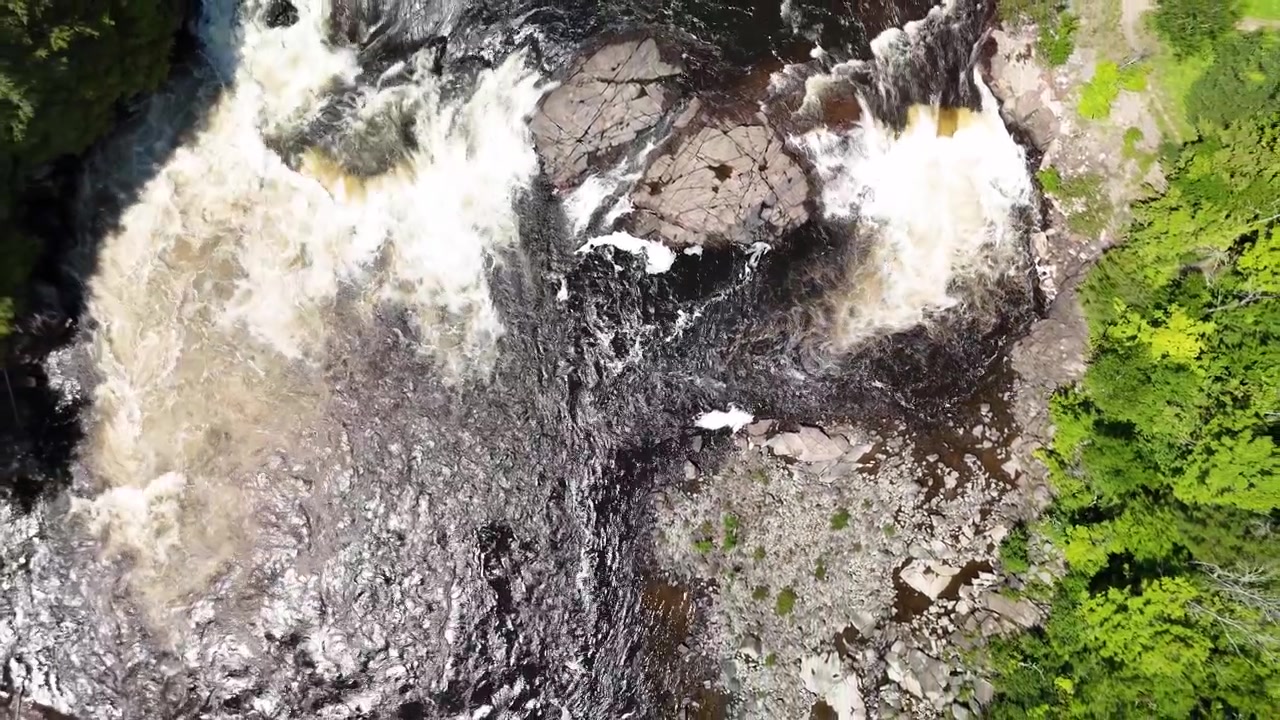 Una ripresa aerea in allontanamento che punta verso il basso su un vortice di un fiume. Durante l'estate.