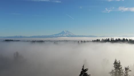 Vuelo-De-Drones-Temprano-En-La-Mañana-Sobre-Campos-De-Niebla-Con-Cielos-Azules-Y-Montañas-En-El-Fondo