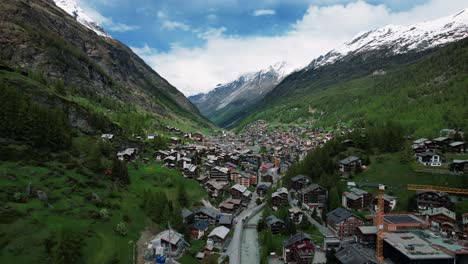 4k drone aerial of town of zermatt nestled in mountain landscape pan tilt to cliff in switzerland