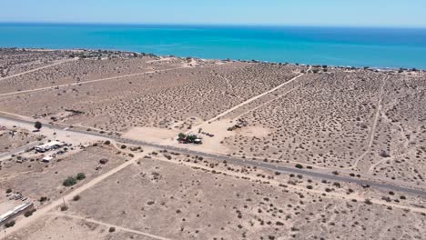 la órbita aérea desciende sobre las dunas de matorrales áridos y arenosos de baja méxico con una impresionante agua azul del océano en la distancia.