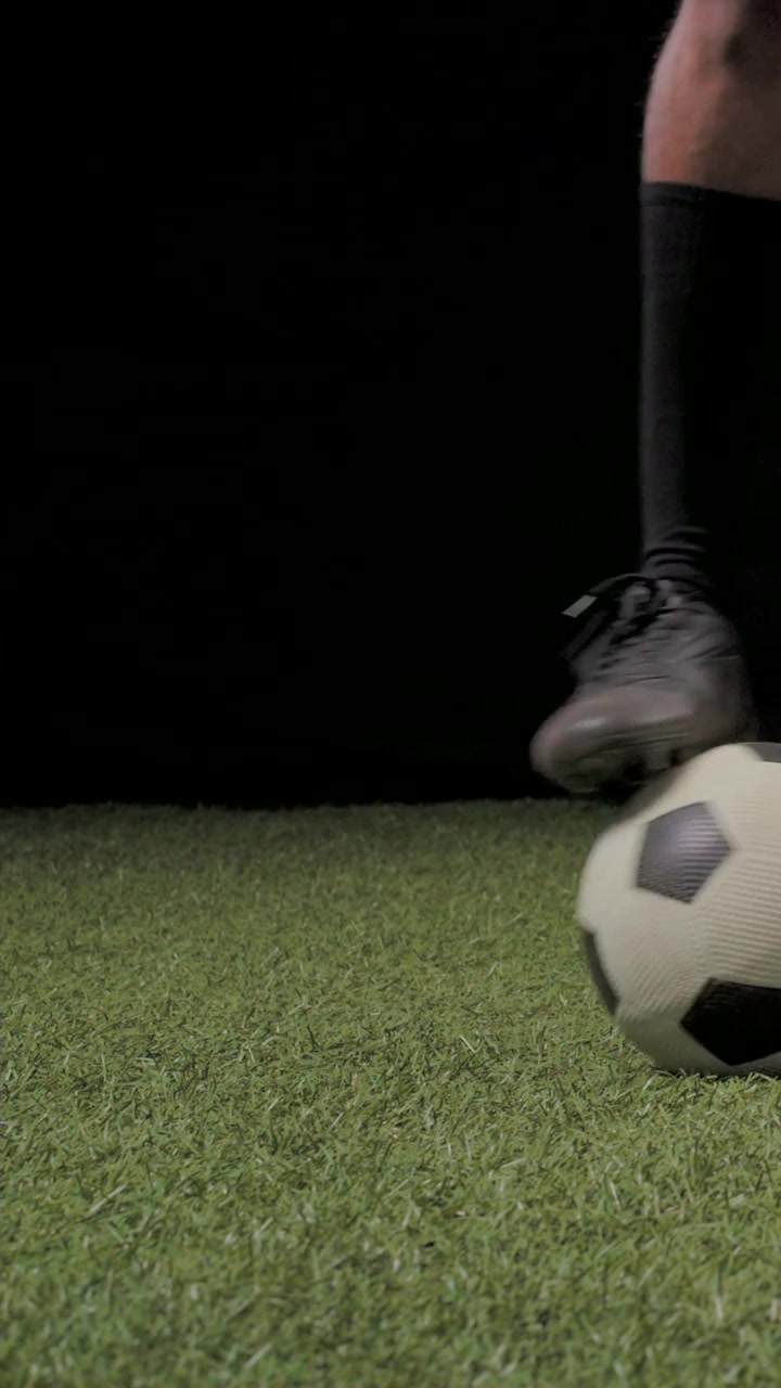 Video vertical: Hombre con tacos comenzando con el balón en los pies, golpeándolo y practicando el control del balón en césped artificial de estudio.