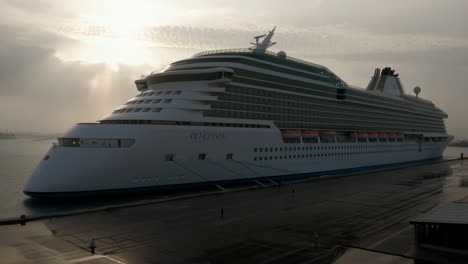 a large cruise ship named "oli ceises" docked at a port under a dramatic sky
