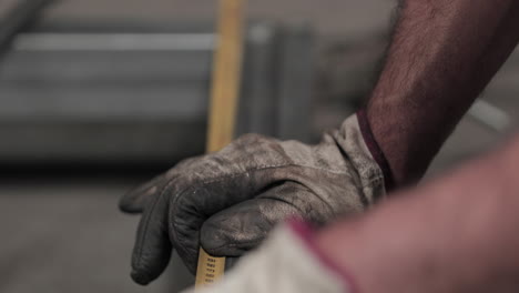 manos con guantes sucios que miden el marco tubular con una cinta métrica - enfoque en rack, cámara lenta