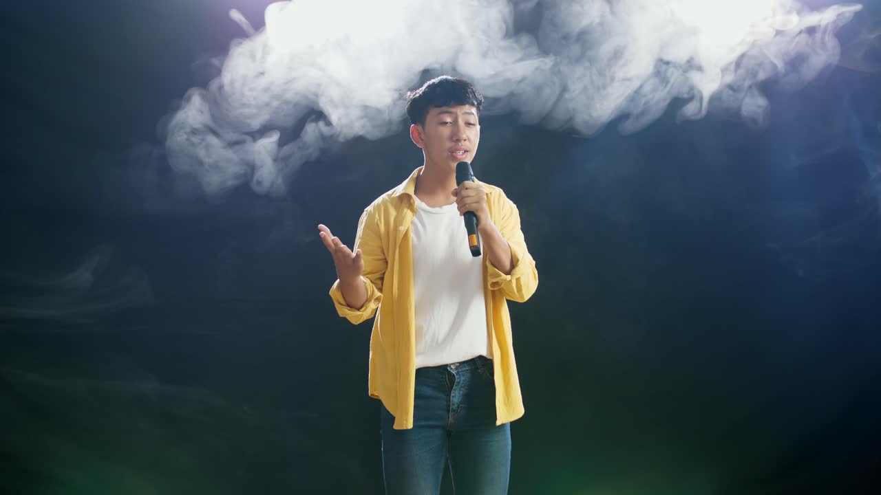 젊은 아시아 소년은 마이크를 들고  연기가 검은 바탕에 노래