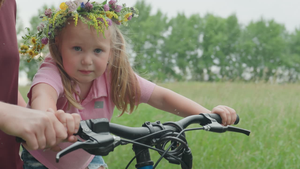 Dziewczynka ćwiczy jazdę na rowerze pod okiem instruktora, dziewczynka rasy kaukaskiej doskonali swoje umiejętności jazdy dzięki wsparciu rodziców, młoda dziewczyna uczy się jeździć na rowerze na łące, a rodzice zapewniają pomoc i wsparcie